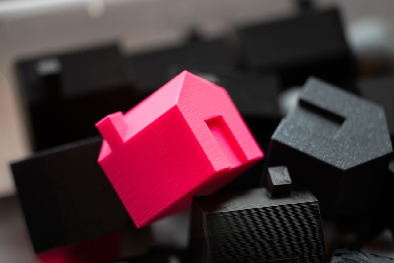 A bright pink house model stands out against a background of black blocks, symbolizing real estate uniqueness.
