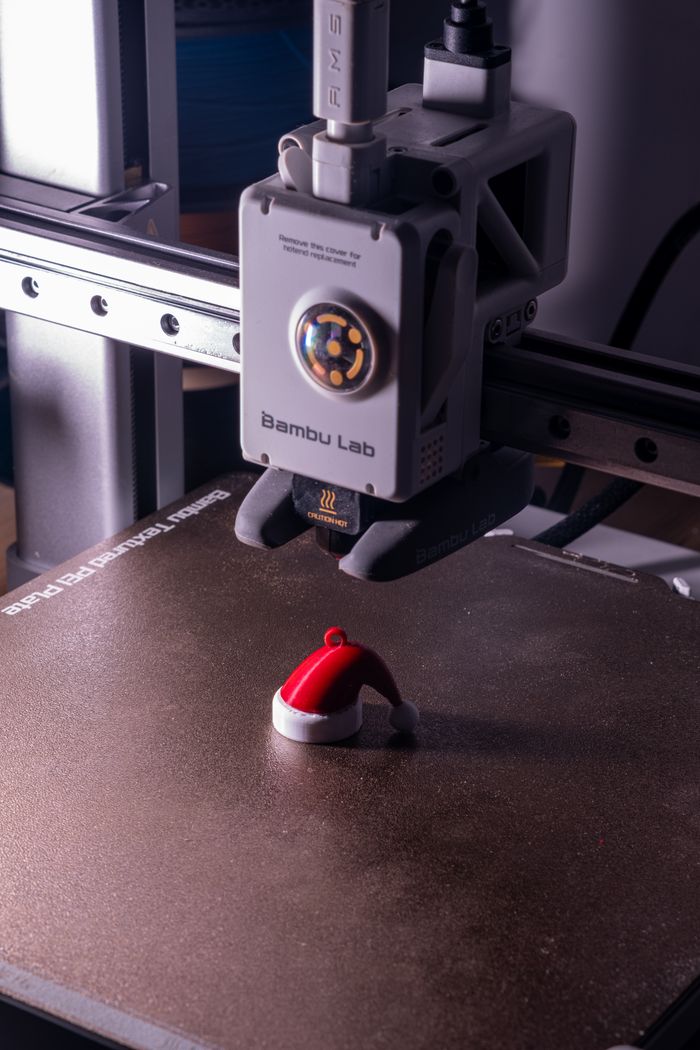 Home 3D printer crafting a small Santa hat ornament, showcasing holiday-themed technology.